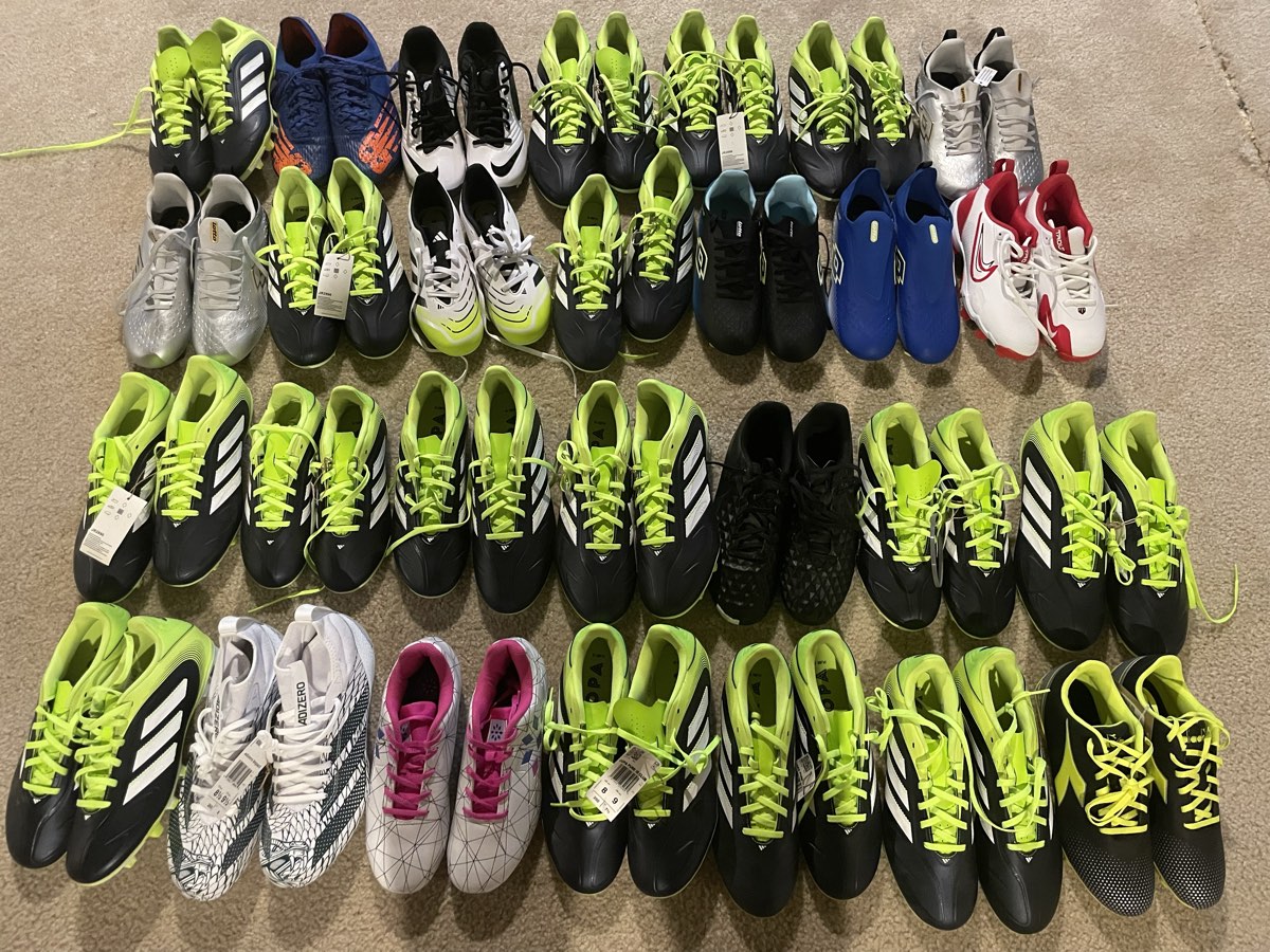 Dozens of pairs of football boots laid out in rows on the ground, sorted before shipping