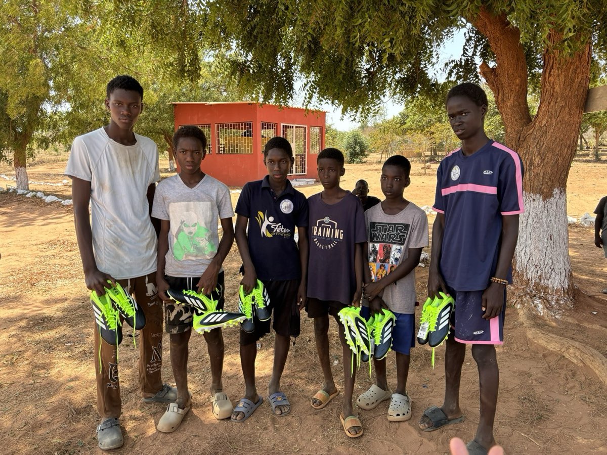 Six boys standing under a tree, each holding a new pair of football boots